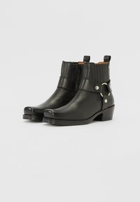 Botas de cuero negro hasta el tobillo con cremallera, paneles laterales texturizados, una correa y acentos metálicos, y un tacón bajo. Acabado suave y punta redondeada.