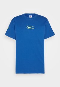 Modré bavlněné tričko s krátkým rukávem. Na hrudi se nachází žluté logo Nike a menší logo je na levém rukávu.