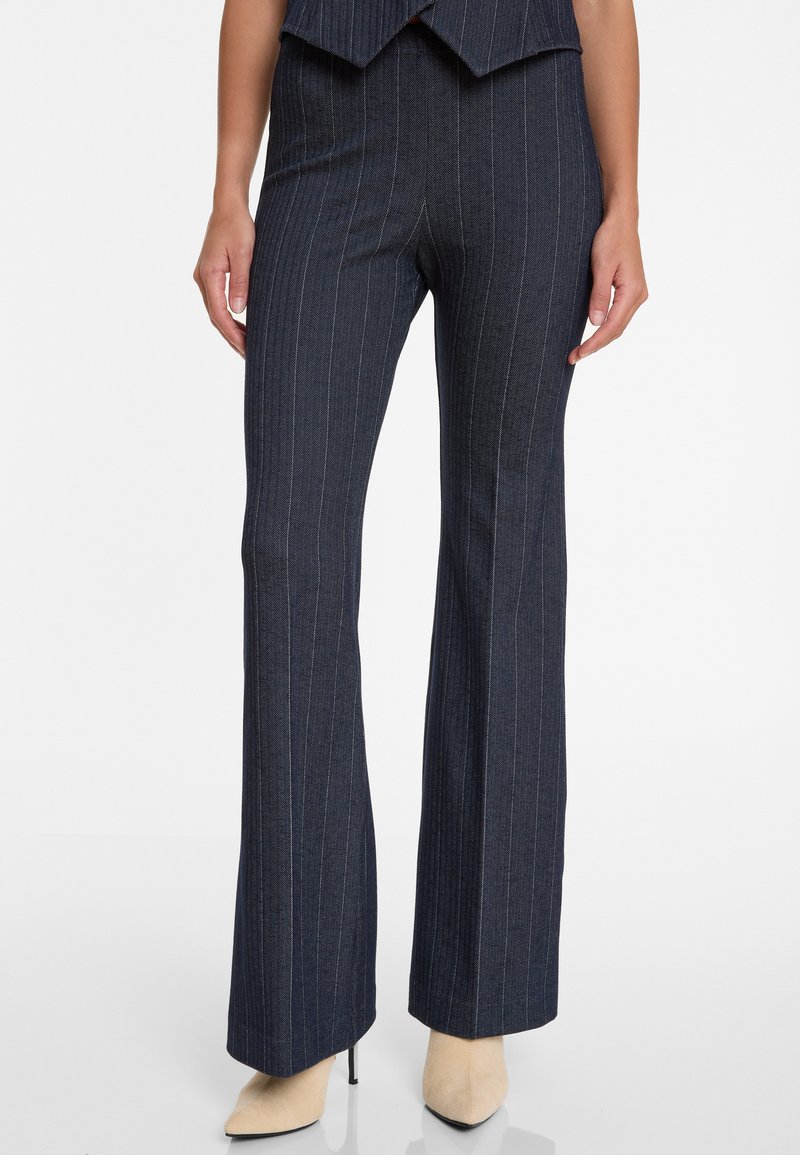 Marineblaue Hosen mit Nadelstreifen, maßgeschneiderter Passform, ausgestellten Beinen und subtiler Textur. Kombiniert mit cremefarbenen spitzen High Heels.