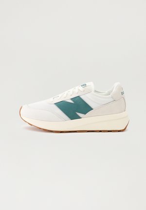 Weißer Sportschuh mit türkisfarbenem "N"-Logo, beigen Wildleder-Akzenten, weißen Schnürsenkeln und hellbrauner Sohle vor schlichtem hellem Hintergrund.