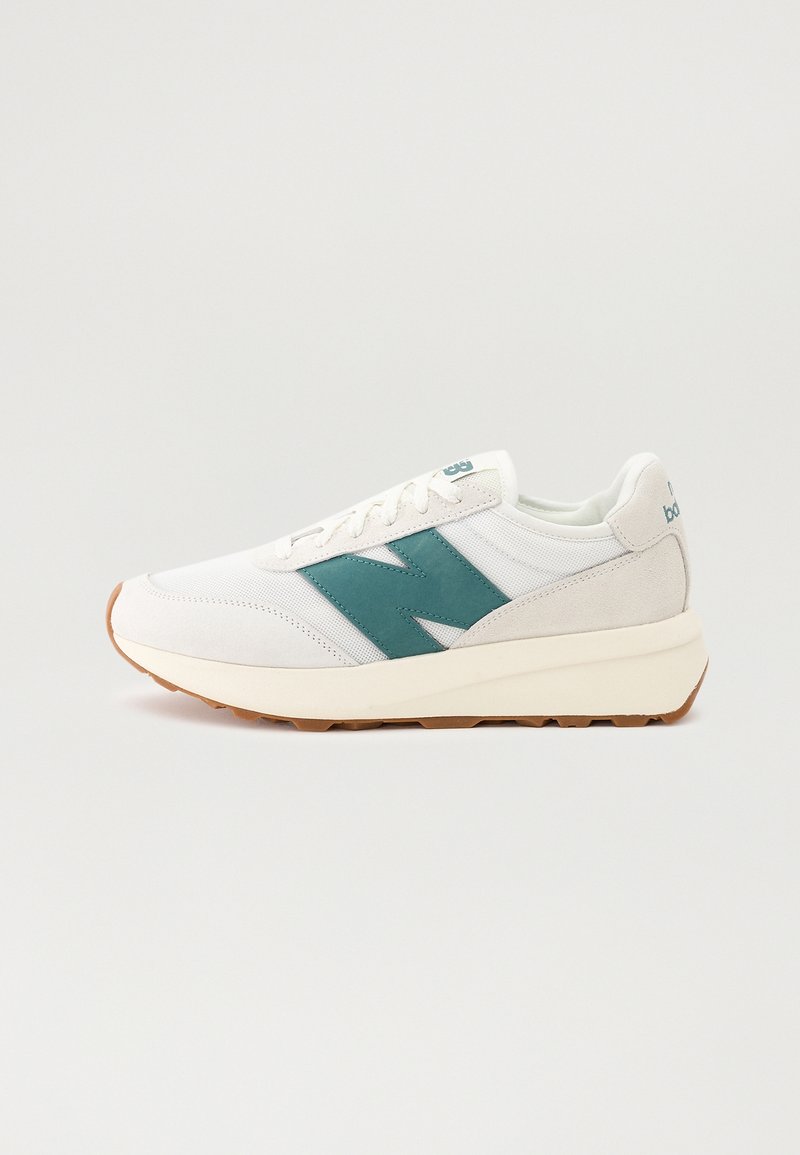 Baskets blanches avec logo "N" turquoise, détails en daim beige, lacets blancs et semelle marron clair sur fond uni clair.