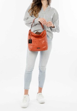 Sac seau en cuir orange texturé avec un haut incurvé et une sangle courte ; présente une étiquette noire et un détail de logo subtil.