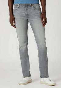 Jeans de mezclilla gris con corte recto, diseño de cinco bolsillos, desvanecimiento sutil y remaches de cobre, combinados con zapatillas blancas.