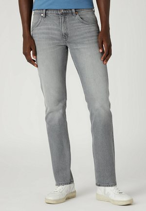 Jeans de mezclilla gris con corte recto, diseño de cinco bolsillos, desvanecimiento sutil y remaches de cobre, combinados con zapatillas blancas.
