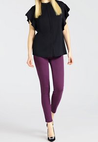 Blusa nera a maniche corte con maniche arricciate, abbinata a jeans viola slim-fit e tacchi alti neri. Nessun motivo o accento visibile.