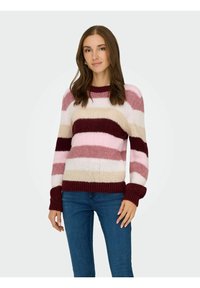 Sweter w paski z różowym, beżowym i burgundowym kolorem. Okrągły dekolt z prążkowanymi mankietami i dołem. Miękka tekstura. Połączony z niebieskimi dżinsami.
