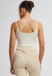 Krémový crop top s tenkými ramienkami, s hladkým povrchom. Skombinovaný so svetlo béžovými rebrovanými nohavicami, ktoré majú priliehavý pás.