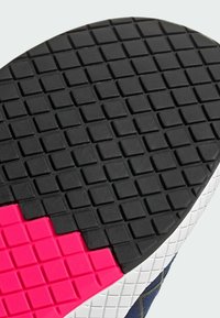 Černá gumová podrážka boty s texturovaným povrchem, zdobená malými čtvercovými vzory a růžovým akcentem na jedné straně.