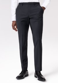Pantaloni grigi scuri su misura realizzati in tessuto liscio, con un design a frontale piatto, tasche laterali e una vestibilità slim, abbinati a scarpe nere.