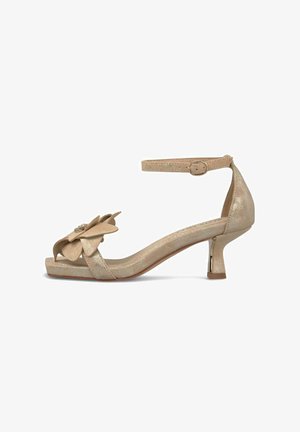 Sandalia beige con punta abierta y tira en el tobillo, tacón bajo curvado y flor decorativa en capas con acento de joya en la tira delantera.