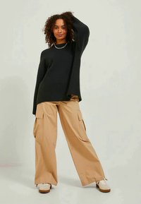 Ylipitkä musta ribbikuvioinen neule yhdistettynä löysiin vaaleanbeigeihin cargo-housuihin, joissa on sivutaskut ja rento istuvuus; käytetään valkoisten lenkkarien kanssa.