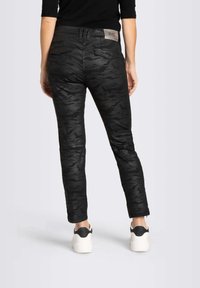 Pantalones de camuflaje negro con corte slim, con un bolsillo trasero y un parche con logo en la cintura. Combinados con zapatillas blancas y negras.