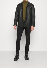 Svart läderjacka med krage och knappstängning. Olivgrön turtleneck under. Slim fit svarta jeans och svarta ankelstövlar.