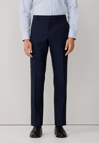 Pantalons de costume bleu marine à coupe droite, texture lisse et plis à l'avant. Associés à une chemise rayée bleu clair et des chaussures noires.