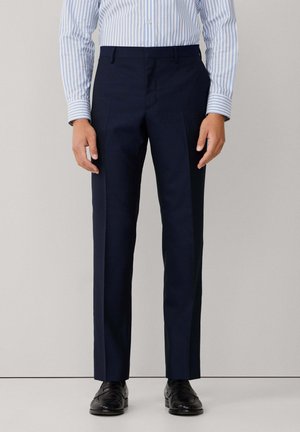 Pantalons de costume bleu marine à coupe droite, texture lisse et plis à l'avant. Associés à une chemise rayée bleu clair et des chaussures noires.
