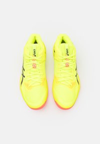Zapatillas deportivas de color amarillo brillante con acentos en negro, parte superior texturizada, diseño de malla y suela en color rosa-naranja, con un sistema de cordones tradicional.