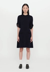 Robe bleu marine à manches courtes avec deux poches avant, une silhouette décontractée, des manches roulées contrastantes et une texture tricot lisse.