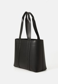 Sac fourre-tout en cuir noir avec doubles poignées et logo "HUGO" en relief sur les bandoulières, présenté sur un fond blanc uni.