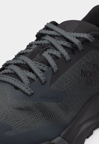 Σκούρο γκρι παπούτσι για τρέξιμο σε μονοπάτια με παχιά υφή στα κορδόνια, επάνω μέρος από δίχτυ και την επωνυμία «The North Face Enduris 4» στην πλευρά.