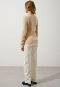 Beige eng anliegender Pullover mit langen Ärmeln, weicher Textur und rundem Ausschnitt, kombiniert mit lockeren, off-white Hosen und dunkelblauen klobigen Absatzschuhen.