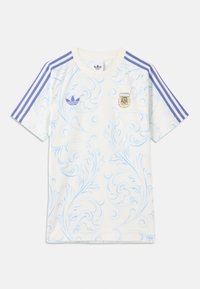 Biely športový dres s krátkym rukávom so svetlomodrým vírivým vzorom, fialovými pruhmi Adidas na ramenách a erbom Argentínskej futbalovej asociácie.