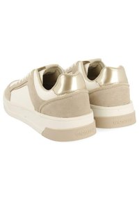 Zapatillas beige con un diseño de ante y cuero liso, que cuentan con un acento metálico dorado en el talón y una suela de goma. Logotipo de la marca en el lado.