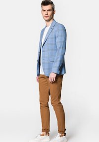 Jasnoniebieska marynarka w kratę z klapami, zestawiona z białym t-shirtem i brązowymi spodniami typu slim fit. Całość dopełniają białe sneakersy.