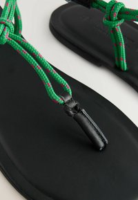 Zwarte platte sandalen met groene en roze gevlochten banden, een gladde matte afwerking en leren accenten voor extra duurzaamheid.