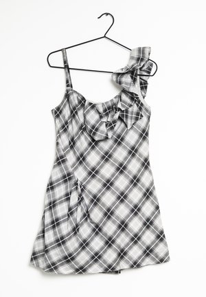 Robe à carreaux noir et blanc avec bretelles volantées, tissu léger, bretelles spaghetti et ourlet évasé. Suspendue à un cintre en métal noir.