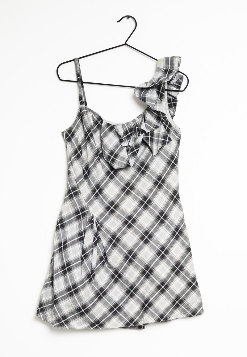 Robe à carreaux noir et blanc avec bretelles volantées, tissu léger, bretelles spaghetti et ourlet évasé. Suspendue à un cintre en métal noir.