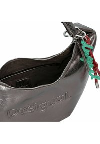Bolso de hombro gris metálico con el texto "Desigual" en relieve, textura suave, cierre de cremallera y detalle de charm colorido sujeto a la correa.