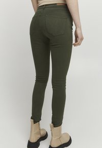 Zelené skinny džíny z hladkého, pružného materiálu mají dvě zadní kapsy a jsou zkombinovány s béžovými kotníkovými botami s robustní podrážkou.