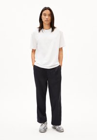 Witte t-shirt met korte mouwen gecombineerd met zwarte broek en grijze sneakers. De outfit heeft eenvoudige, strakke lijnen en een relaxte pasvorm.