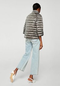 Toppauksellinen hopeanvärinen metallinhohtoinen takki, jossa pystykaulus, lyhyet hihat ja resoripinta, yhdistetty vaaleansinisiin suoralahkeisiin farkkuihin ja valkoisiin korkokenkiin.