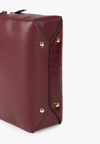 Borsa borgogna con finitura in pelle liscia, dotata di un lato in pelle di serpente rossa con texture e borchie dorate agli angoli.