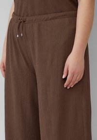 Bruine, getextureerde, loszittende broek met een elastische tailleband, voorzien van een trekkoord en zilverkleurige hardwareaccenten.
