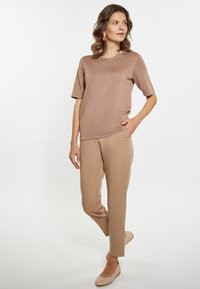 Bruine korte mouw top gecombineerd met beige slim-fit broek. Model draagt lichtbeige flats en toont gladde texturen en neutrale tinten.