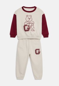 Loungewear sæt i bomuld med en cremet overdel og bordeaux ærmer. Sættet har et bjørngrafik og 'GAP' tekst på toppen; 'G' logo på bukserne.
