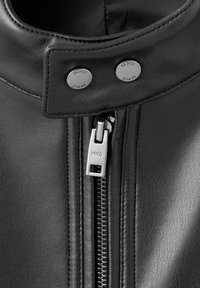 Czarna skórzana kurtka z kołnierzem typu stójka, srebrnymi zatrzaskami i przednim zamkiem błyskawicznym z ozdobnym suwakem z logo. Gładka faktura i staranne przeszycia.