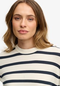 Granatowo-biały sweter w paski z okrągłym dekoltem i teksturowanym splotem, z guzikami na ramieniu jako dodatkowym detalem.