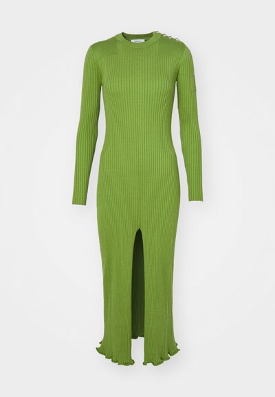 Πράσινο φόρεμα με ριμπ ύφανση, μακριά μανίκια, στρογγυλή λαιμόκοψη, πλάγιο σκίσιμο και κυματιστό τελείωμα. Διαθέτει διακοσμητικά αξεσουάρ στον ώμο.
