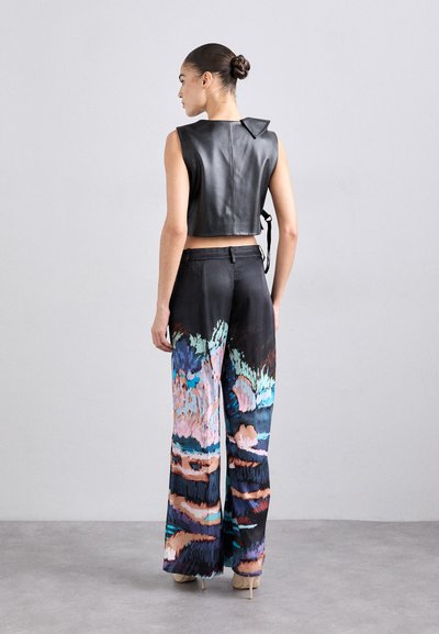 Svart lær cropped vest med spiss krage, sammen med vide bukser med et fargerikt abstrakt mønster i blått, rosa og svart.