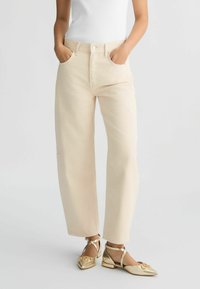 Jean large taille haute beige avec poches avant, associé à des ballerines dorées métalliques avec des brides de cheville et un design à bout pointu.