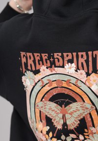 Black hoodie featuring a colorful graphic with the words "FREE SPIRIT," a butterfly, and floral patterns in pastel hues.