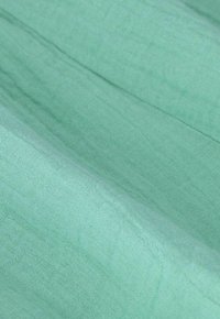 Lichtgroene stof met een zachte, textuurrijke afwerking. Het oppervlak heeft een subtiel weefpatroon, wat de lichte uitstraling versterkt.