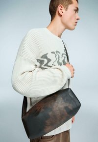 Borsa a tracolla in pelle con una finitura liscia di colore marrone scuro e accenti più chiari. Texture morbida e forma allungata e curvata.