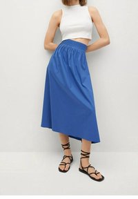 Gonna midi in cotone blu con vita arricciata, design fluido e orlo asimmetrico. Indossata con sandali neri con cinturini.