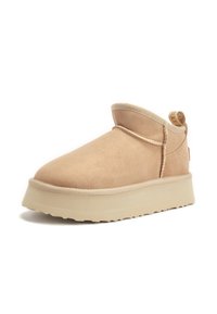 Beige suède enkellaars met een ronde neus, zachte voering, verhoogde stiknaad en een lichtgewicht rubberen zool. Inclusief een klein trekhaakje aan de achterkant.