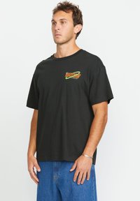 Schwarzes T-Shirt mit kurzen Ärmeln aus Baumwolle, mit einem bunten "Volcom"-Logo auf der Brust, lockerer Schnitt und Rundhalsausschnitt.