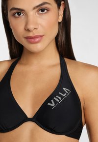 Schwarzer Bikini-Oberteil in dreieckiger Form, mit einem Logo auf der linken Seite und dünnen Trägern. Das Material wirkt glatt und dehnbar.